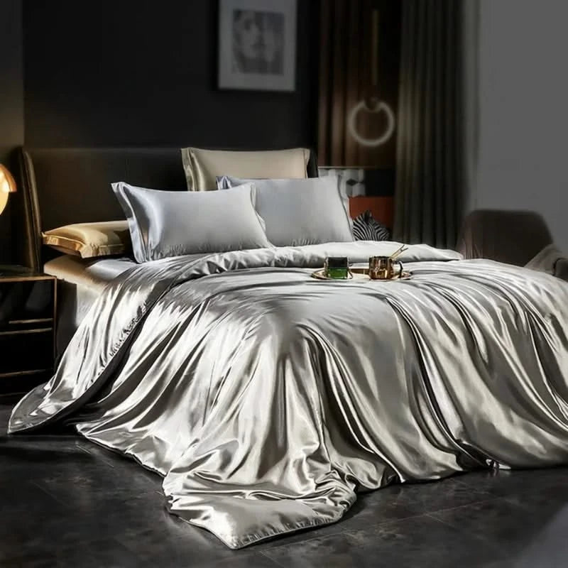 Silver satin bedding set on a bed in a dimly lit room.