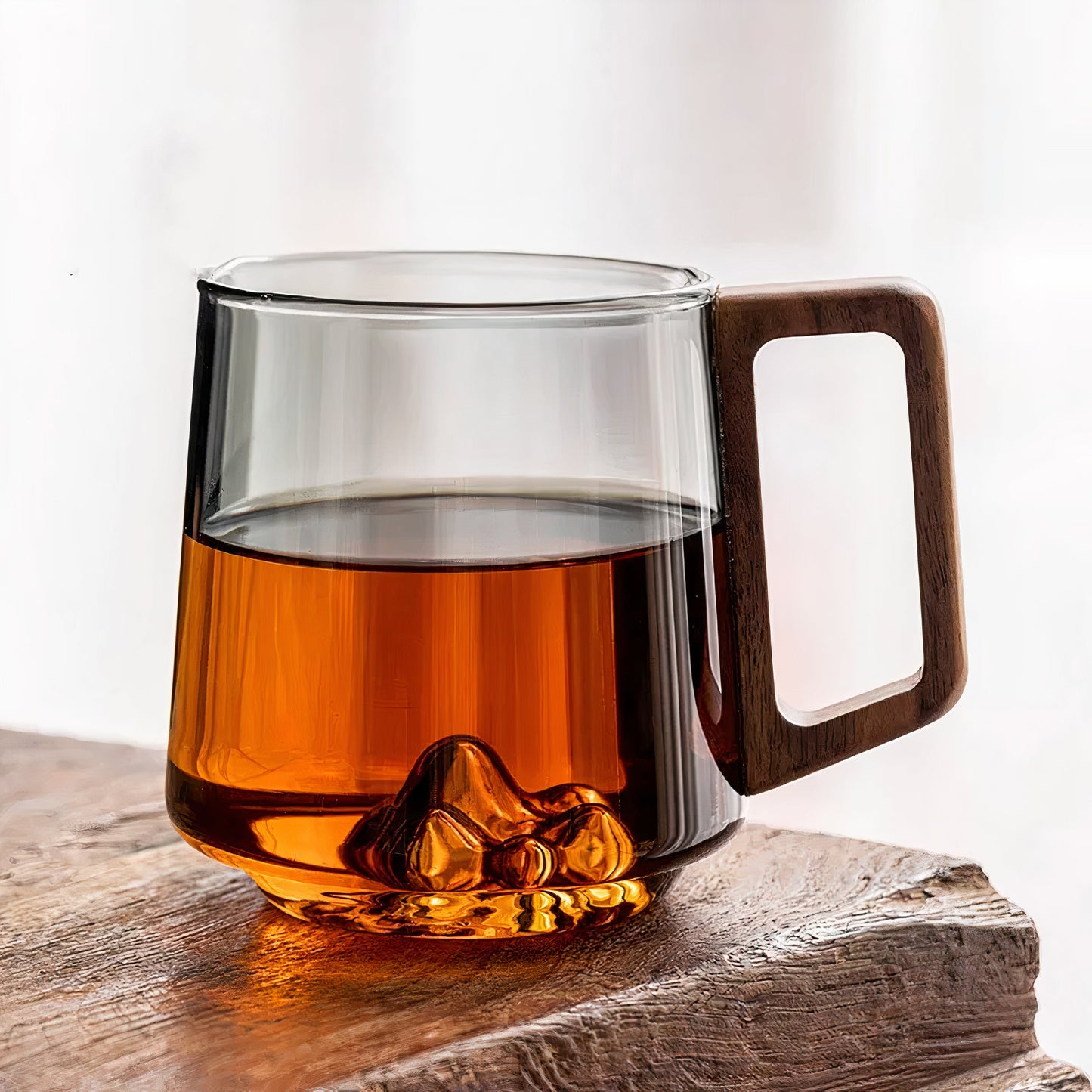 Clear glass mug with wooden handle filled with amber liquid on a wooden surface