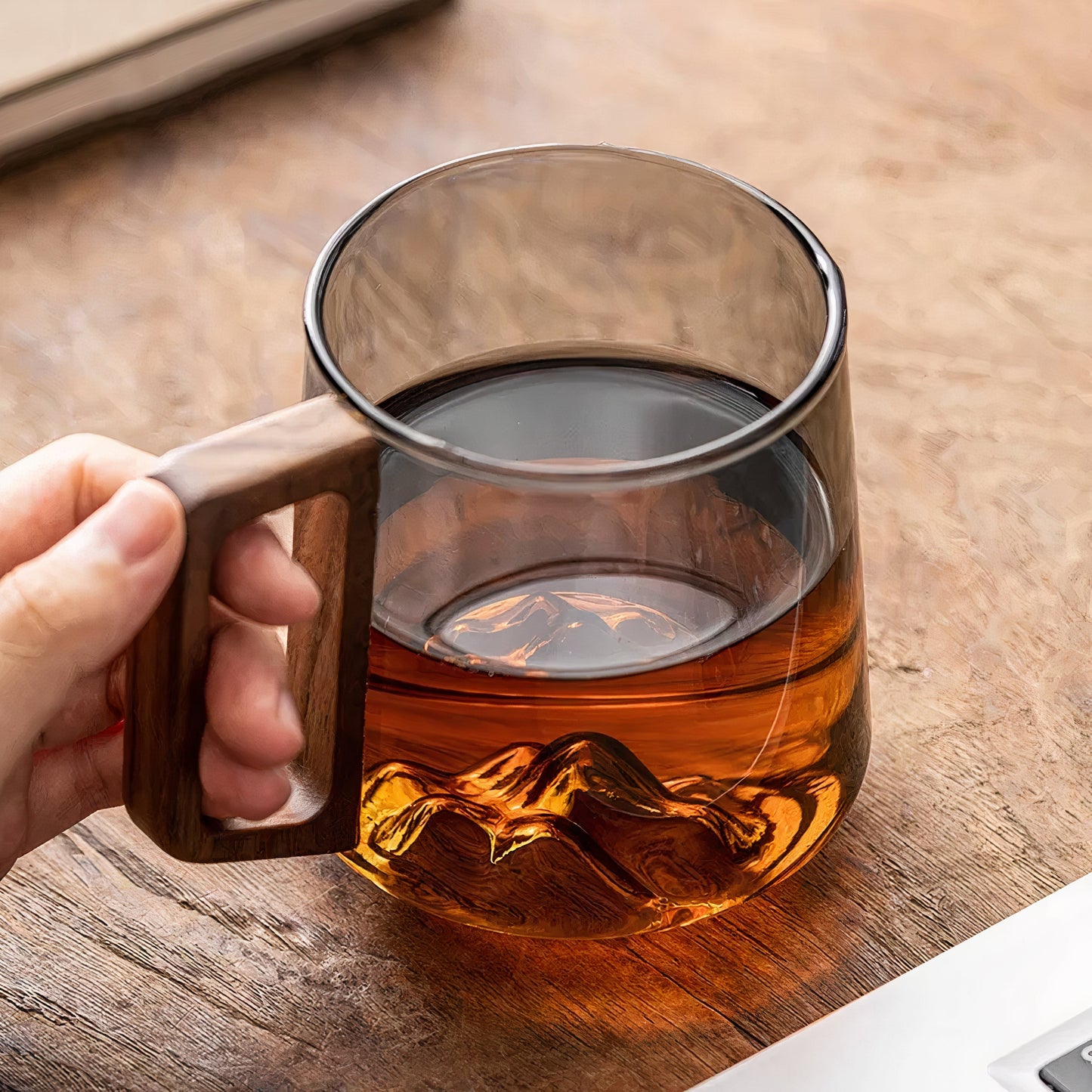 Glass mug with wooden handle filled with tea on a wooden surface