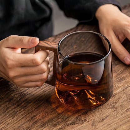 Person holding a wooden mug filled with a dark liquid on a wooden table