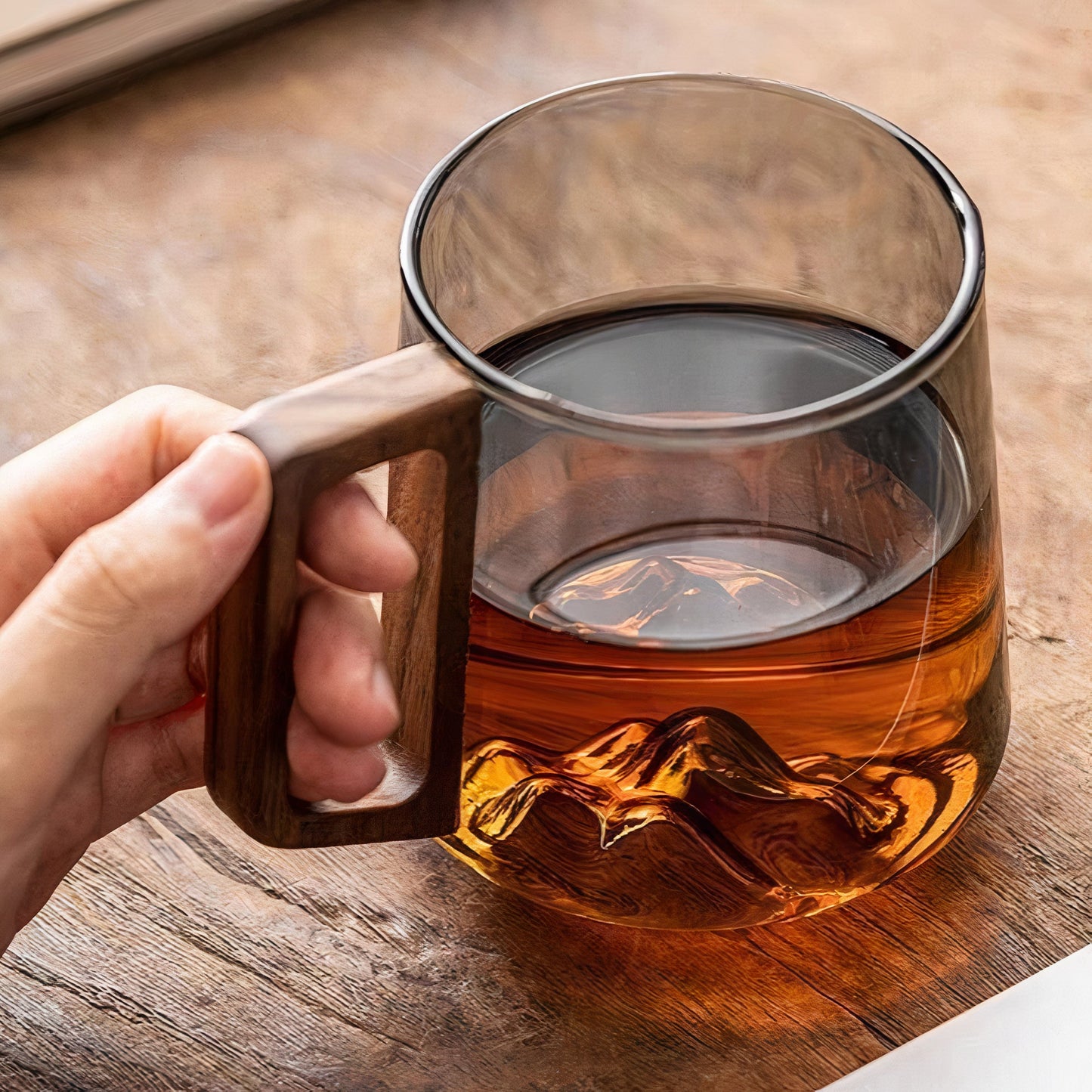 Glass mug with wooden handle filled with tea on a wooden surface
