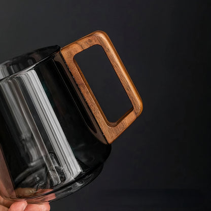 Glass mug with a wooden handle held against a dark background