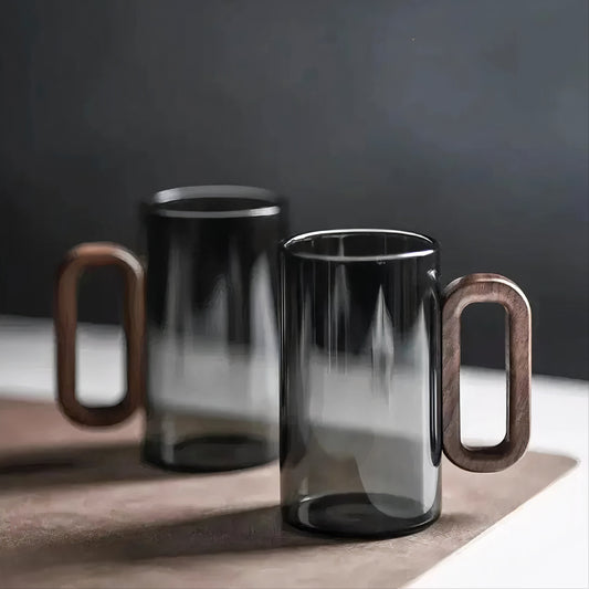 Two black glass mugs with wooden handles on a dark background