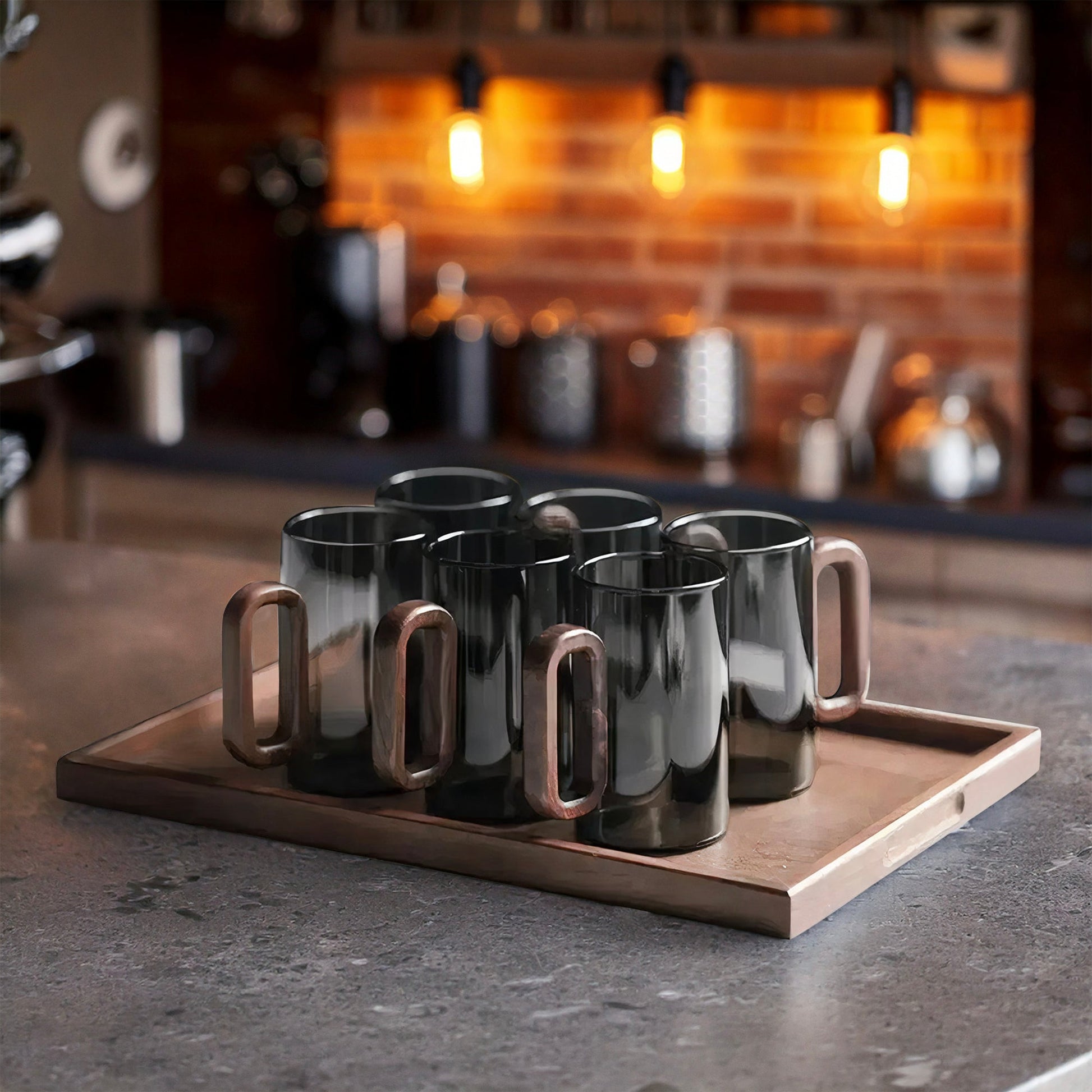 Set of black mugs with bronze handles on a wooden tray in a kitchen setting.