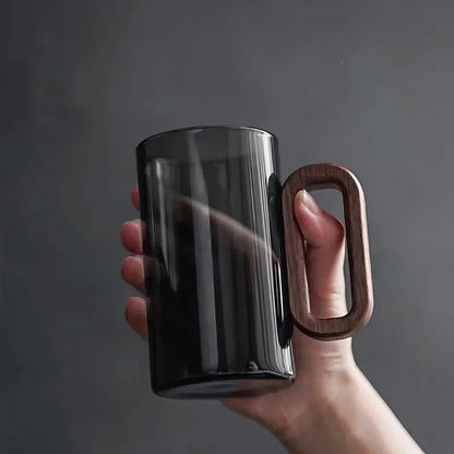Hand holding a black mug with a wooden handle against a dark background