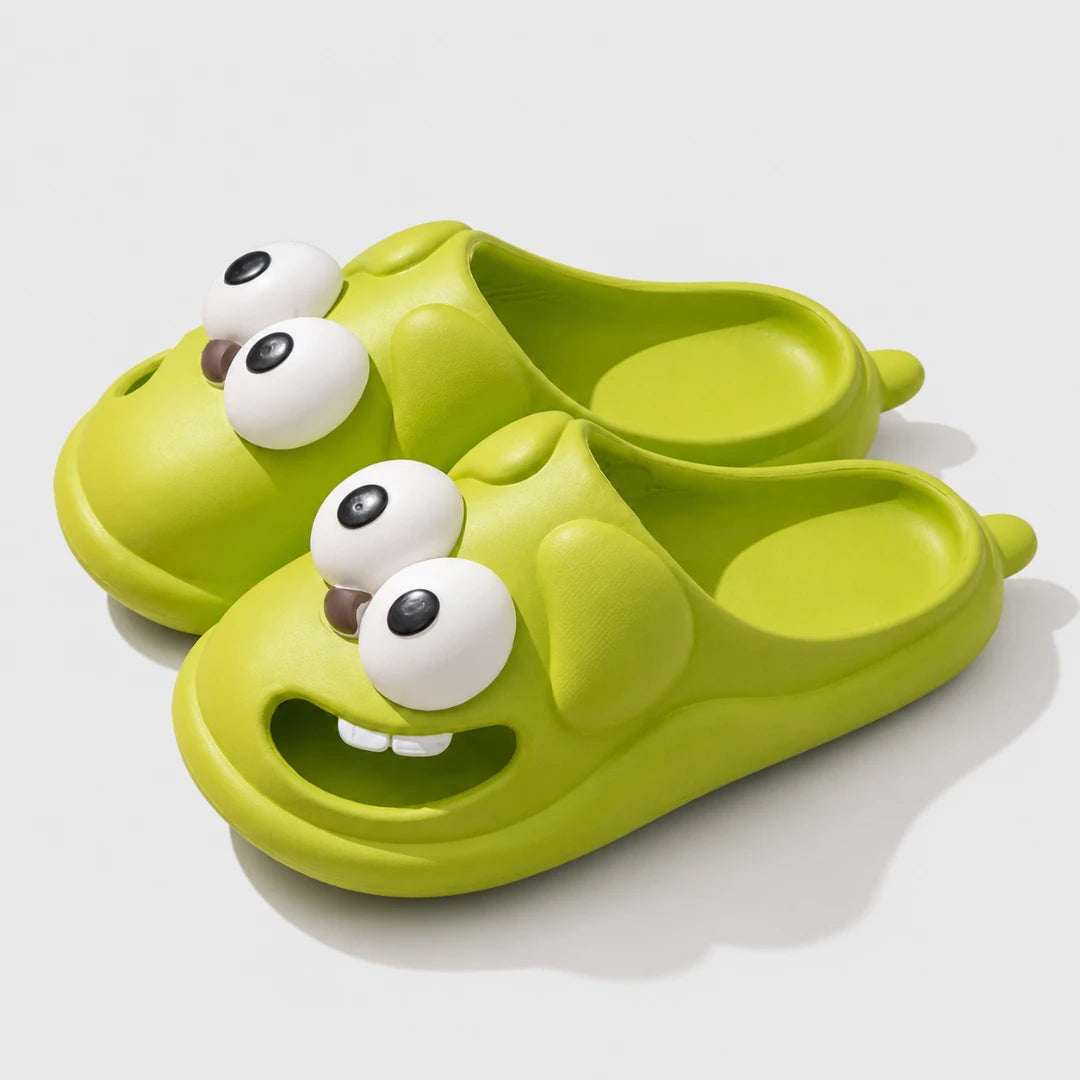 Josh & Tate - SnaggleToe™ Slides - A pair of lime green slip-on slippers shaped like cartoon monster faces with large white eyes and small brown nose details, shown on a light gray background.