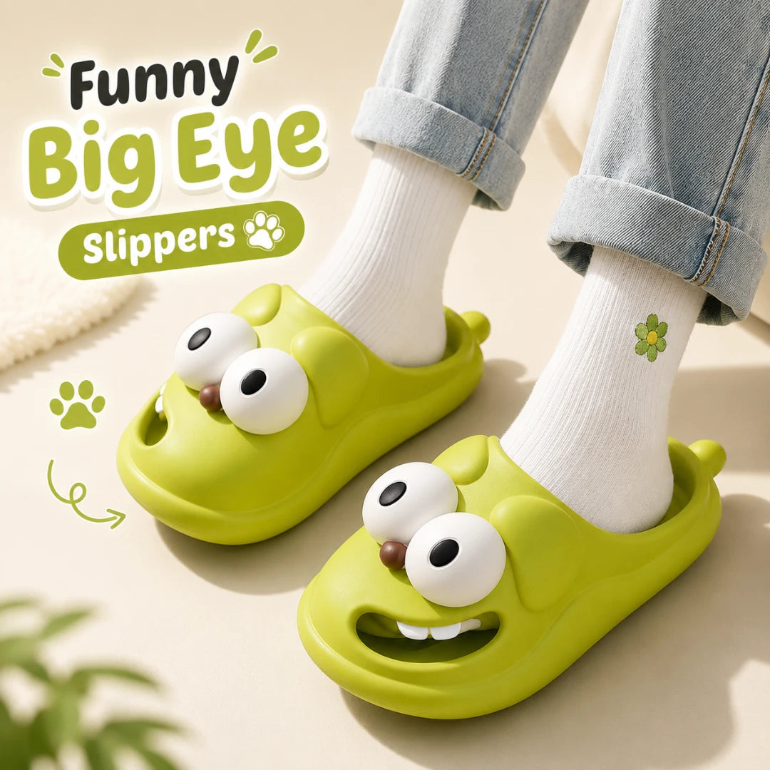Josh & Tate - SnaggleToe™ Slides - A person wearing lime green cartoon-style slip-on slippers with large white eyes and a smiling mouth, paired with white socks and light blue jeans. The image includes promotional text reading 'Funny Big Eye Slippers' and decorative paw-print graphics on a light beige background.