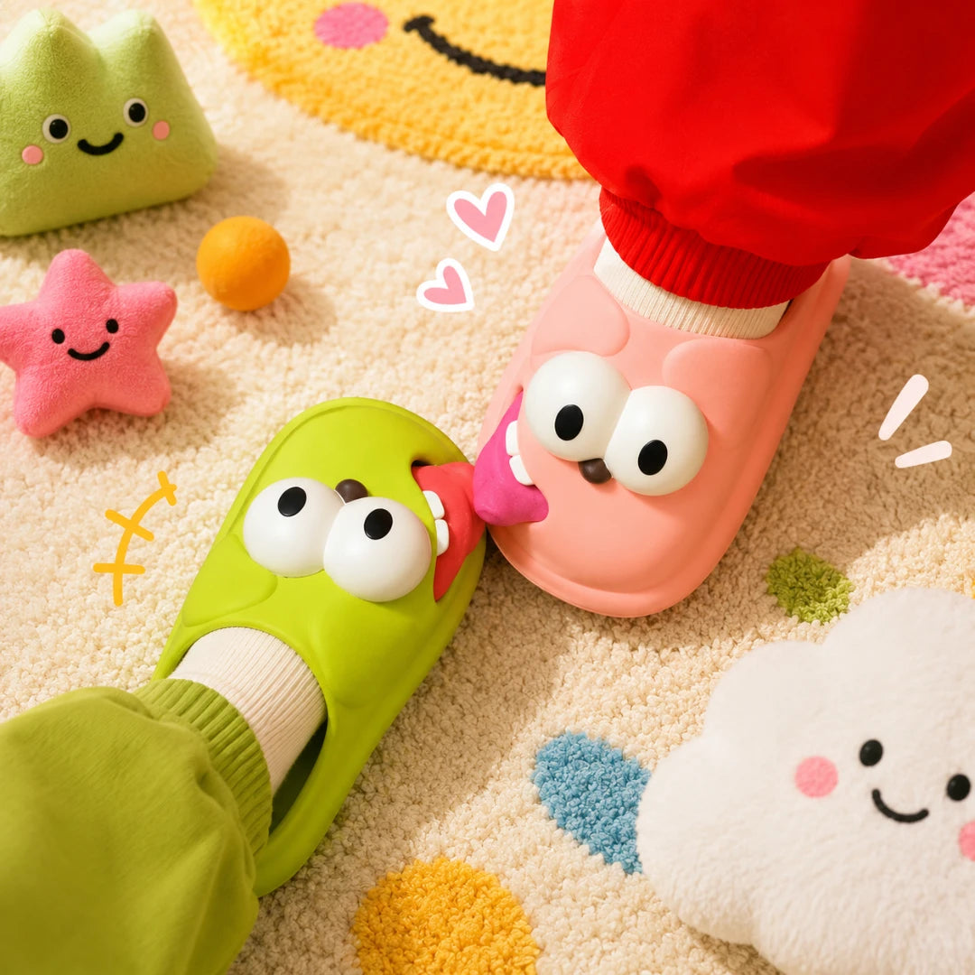 Josh & Tate - SnaggleToe™ Slides - A pair of colorful, cartoon-style slip-on slippers with large eyes and smiling faces, shown being worn with red pants on a soft, playful carpet surrounded by matching plush toys.