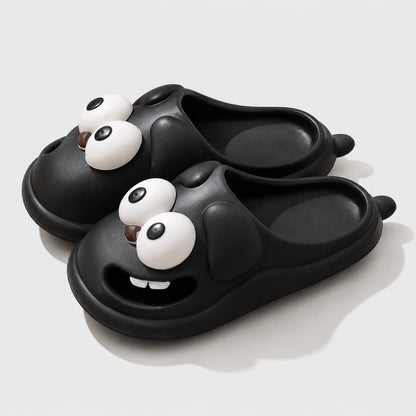Josh & Tate - SnaggleToe™ Slides - A pair of black slide sandals with a cartoon dog face design, featuring large white eyes and a smiling mouth showing small white teeth, set against a light gray background.