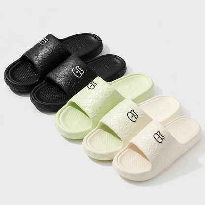 Josh & Tate - SoftBear™ Non-Slip Cushion Slides - Three pairs of slide sandals arranged on a light gray background: black, pale mint green, and off-white. Each sandal has an embossed textured pattern and a small stylized logo on the strap.