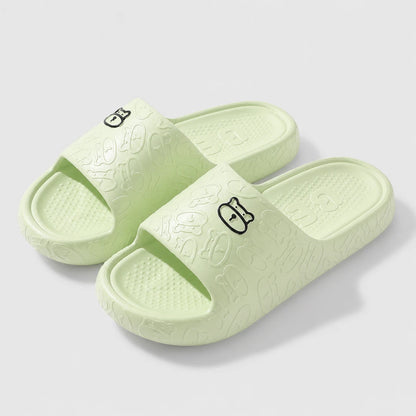 Josh & Tate - SoftBear™ Non-Slip Cushion Slides - A pair of light mint green slide sandals with embossed cartoon patterns and small black cat face logos on the straps, shown on a light gray background.