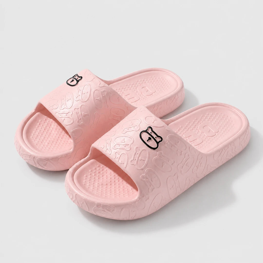 Josh & Tate - SoftBear™ Non-Slip Cushion Slides - A pair of light pink slide sandals with embossed cartoon patterns and small black logo details on the straps, shown on a light gray background.