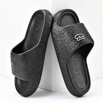 Josh & Tate - SoftBear™ Non-Slip Cushion Slides - A pair of black slide sandals with an embossed cartoon pattern and a small silver logo on the strap, displayed on a white geometric background.