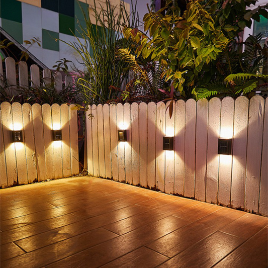 Outdoor setting with wooden fence and wall-mounted lights casting a warm glow.