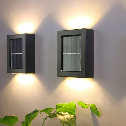 Two solar wall lights on a gray wall with a plant in the foreground.