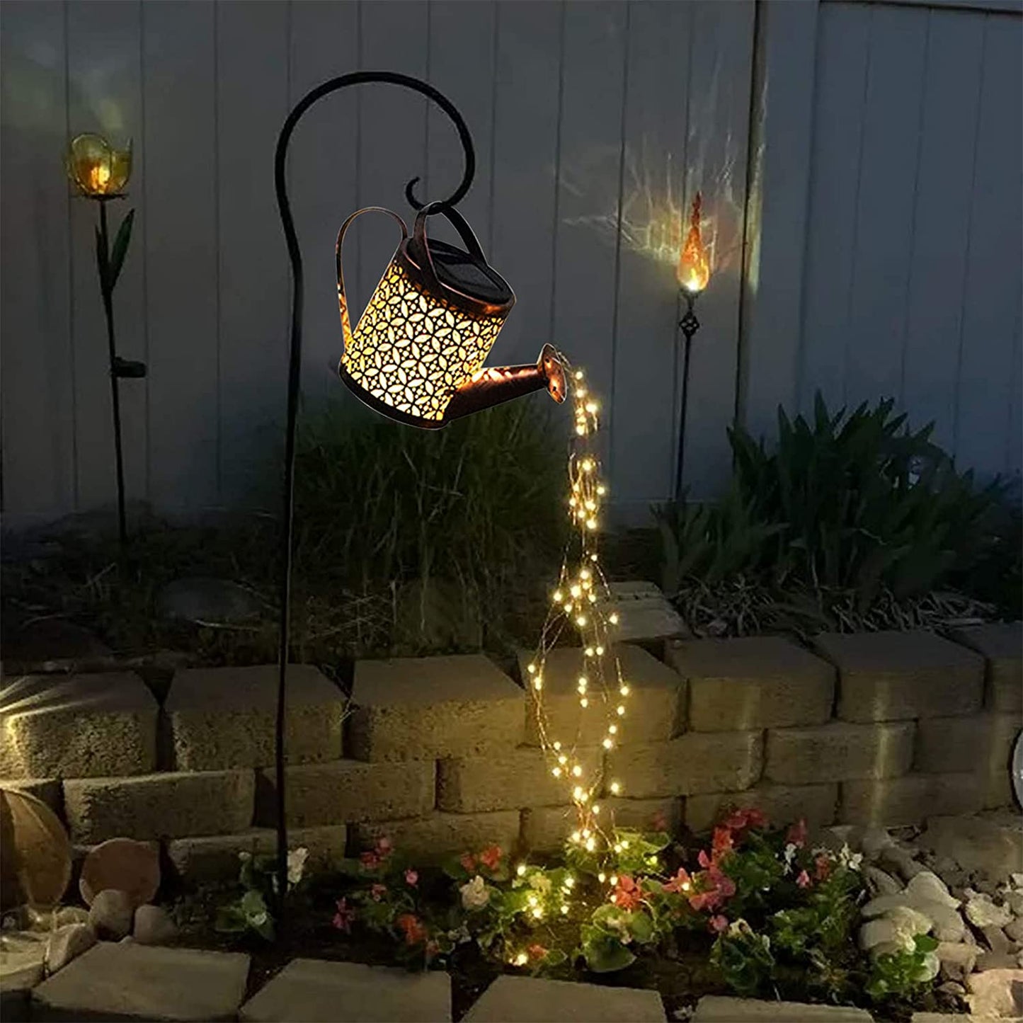 Decorative solar light shaped like a watering can with string lights in a garden setting.