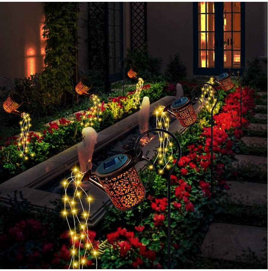 Decorative string lights and lanterns on a garden path with flowers and a building in the background.