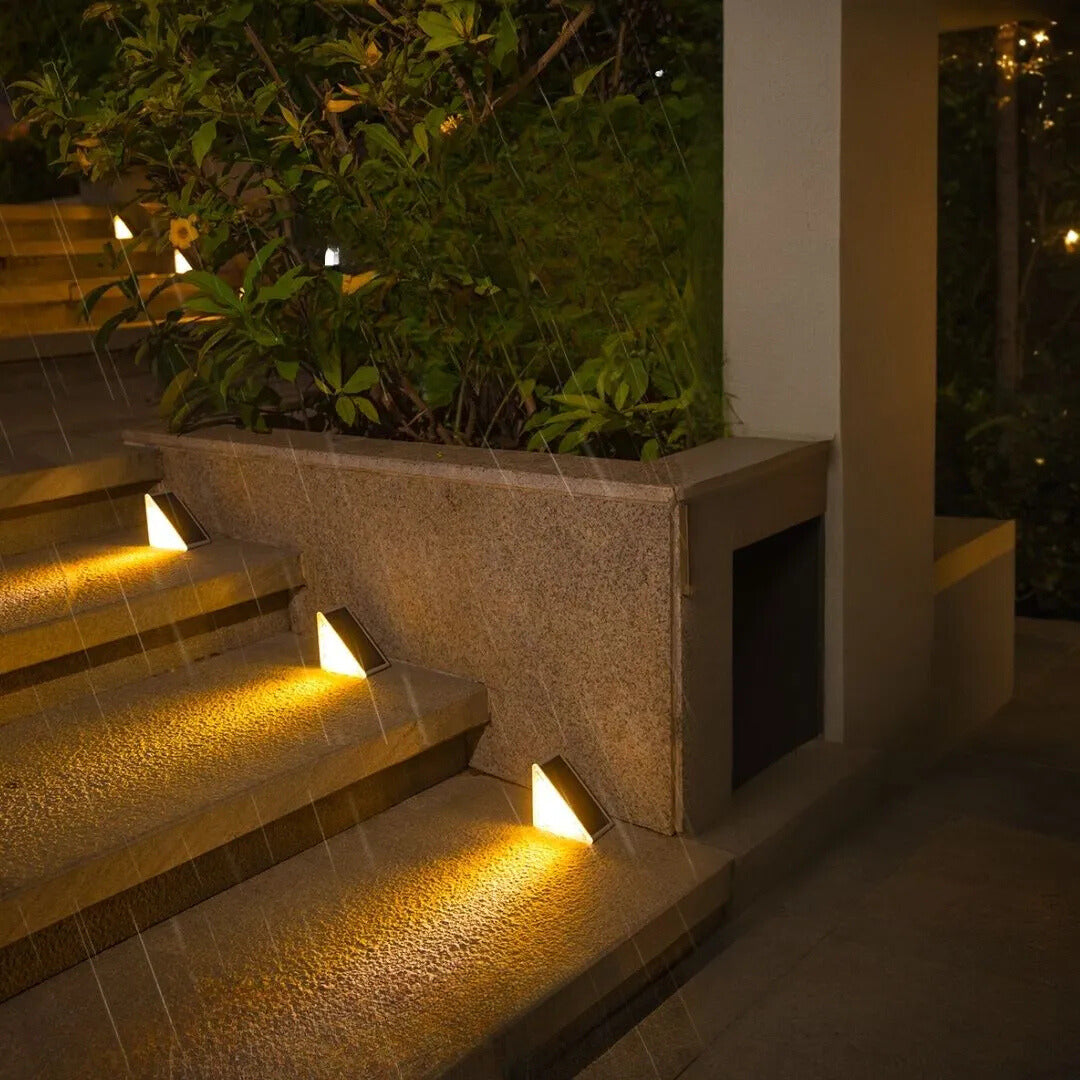 Staircase with embedded lights at night, surrounded by greenery.