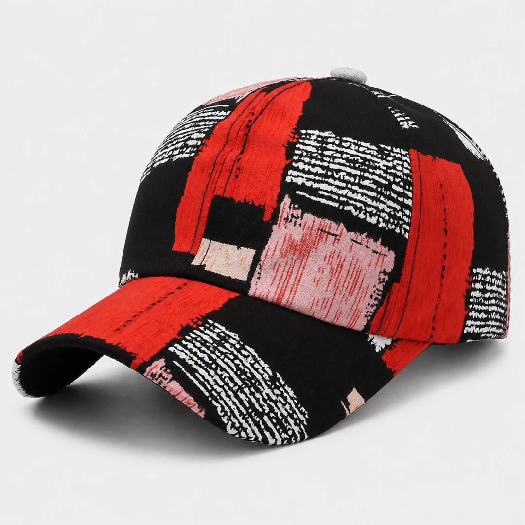Josh & Tate - SplashPatch™ Graffiti Cap - A baseball cap featuring a bold abstract patchwork pattern of red, black, white, and light pink brushstrokes, photographed on a clean light gray background.
