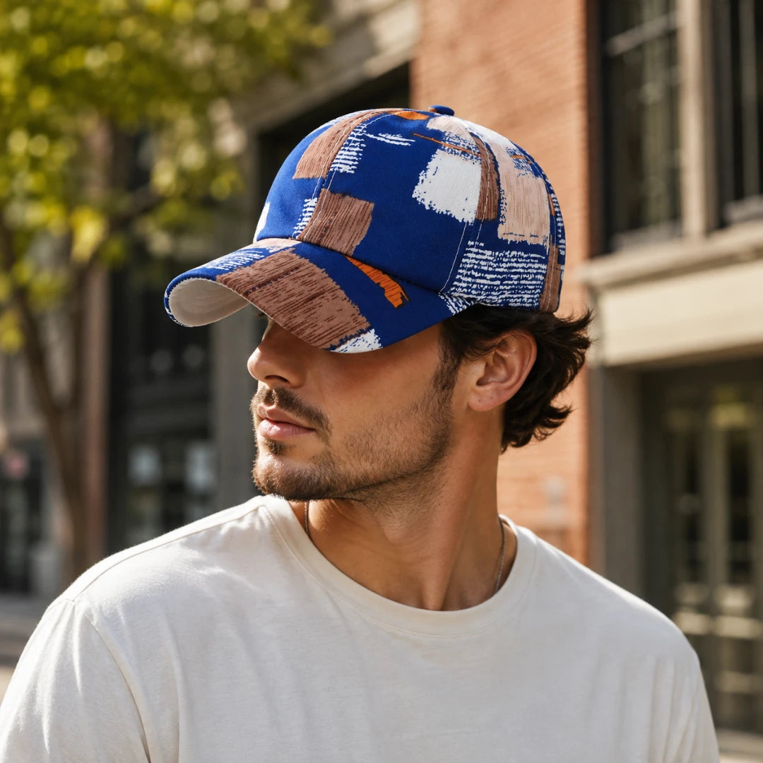 Josh & Tate - SplashPatch™ Graffiti Cap - A man wearing a blue baseball cap with a geometric patchwork pattern in brown, beige, and white, standing outdoors in front of a brick building.