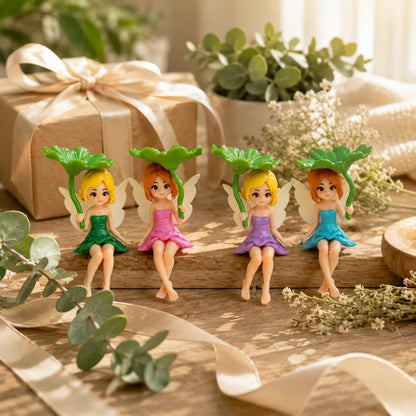 Josh & Tate - SproutPixie™ Leaf Umbrella Pixie Car Ornament - Four small fairy figurines with wings and leaf-shaped heads sit on a wooden surface in a styled setting with a wrapped gift box, ribbon, plants, and dried flowers.