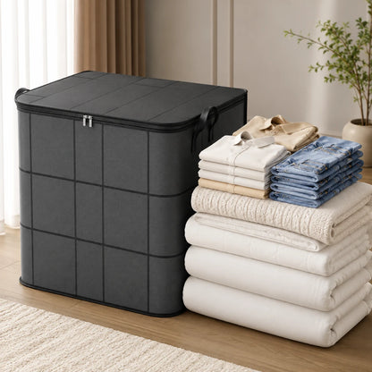 Josh & Tate - StackFold™ Folding Storage Box - A black fabric storage bin with a zip-top lid stands next to a stack of neatly folded white, beige, and blue textiles in a bright indoor room.