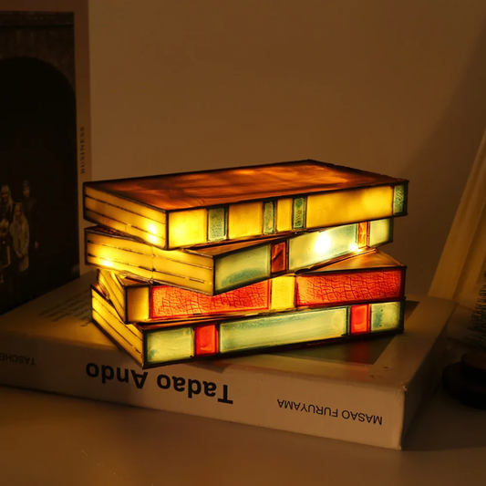 Stack of books illuminated by a lamp with stained glass design on a table.
