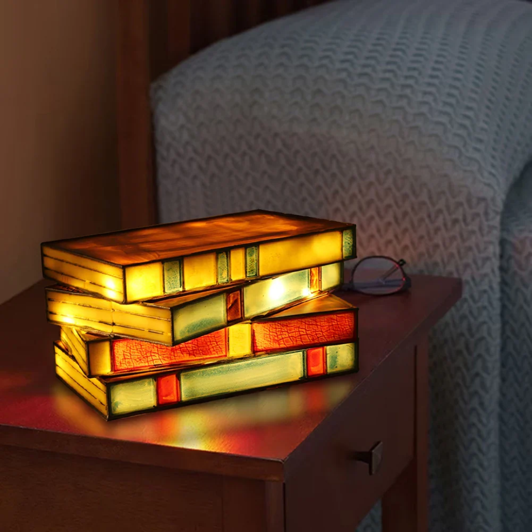 Stack of colorful books illuminated as a lamp on a wooden surface with a blurred chair in the background.