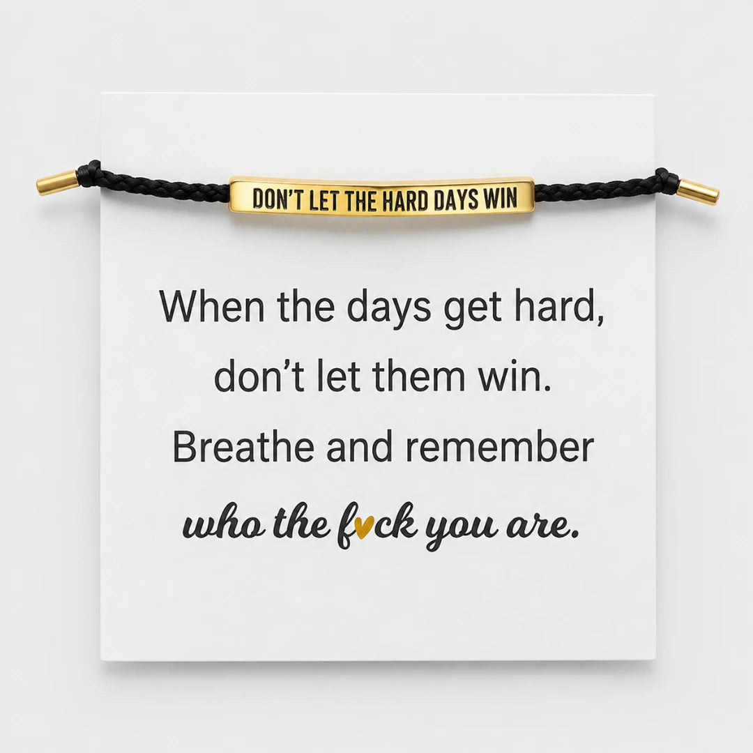 Josh & Tate - StainlessSteel™ Adjustable Bracelet - A black cord bracelet with a gold-toned rectangular bar engraved with the phrase 'DON'T LET THE HARD DAYS WIN' is displayed across a white card. The card also features a motivational quote printed in black text, with the word 'fuck' highlighted in gold.