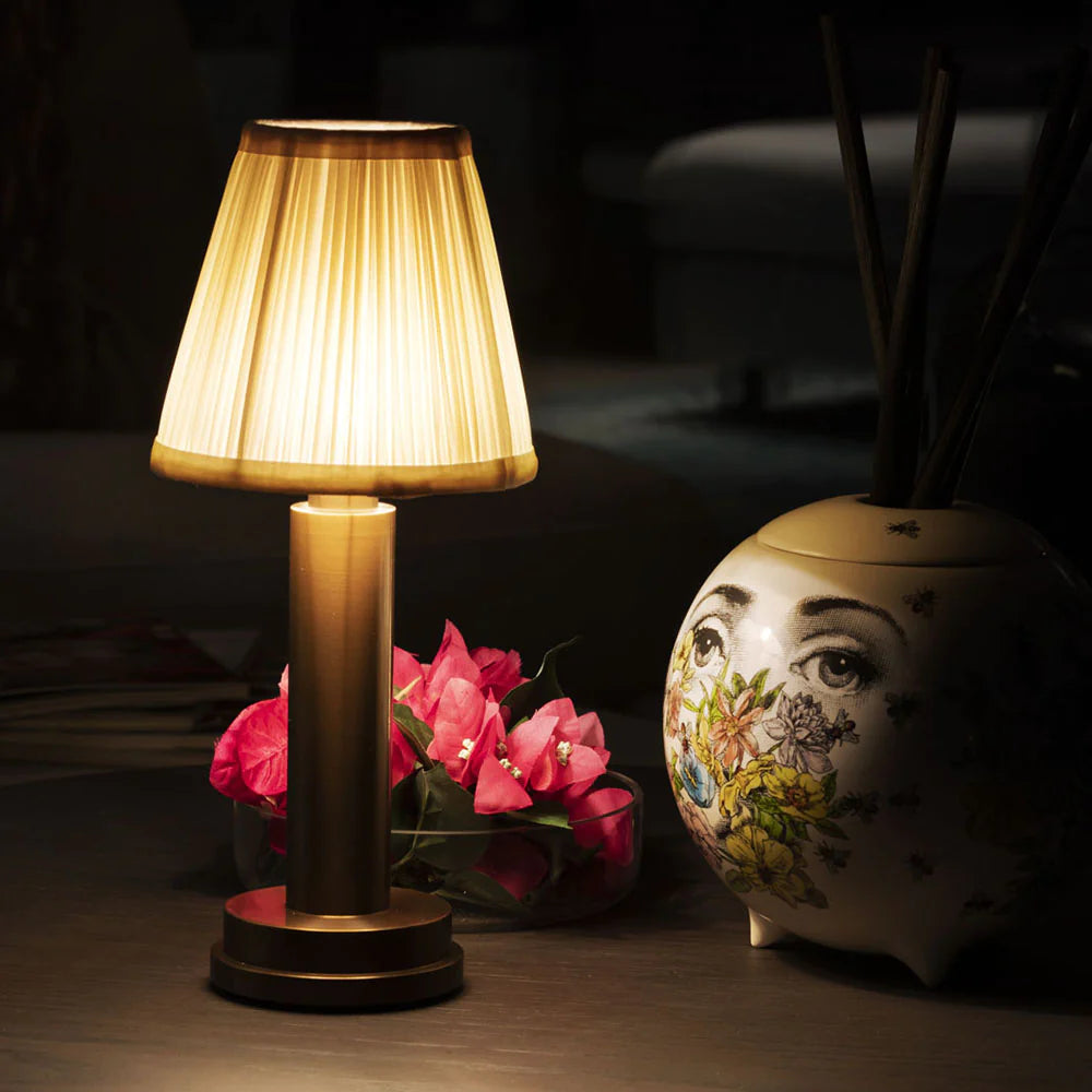 Table lamp with pleated shade next to a decorative vase and pink flowers on a dark background