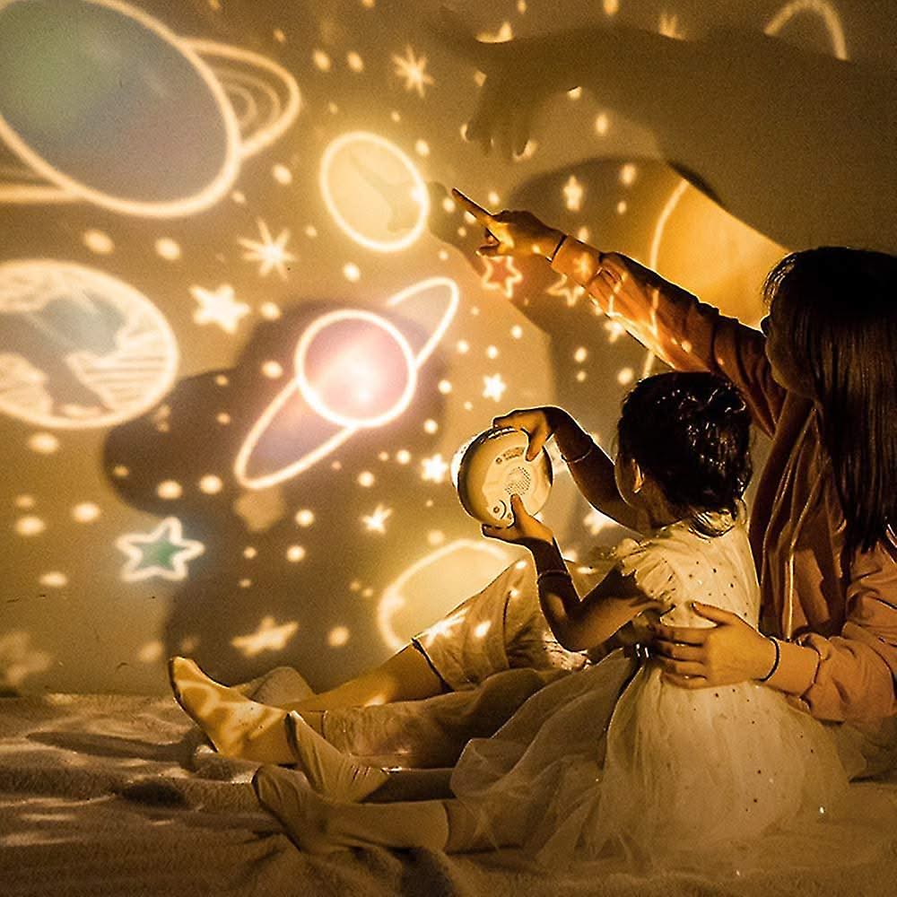 Two children pointing at a starry night sky projection on a wall.