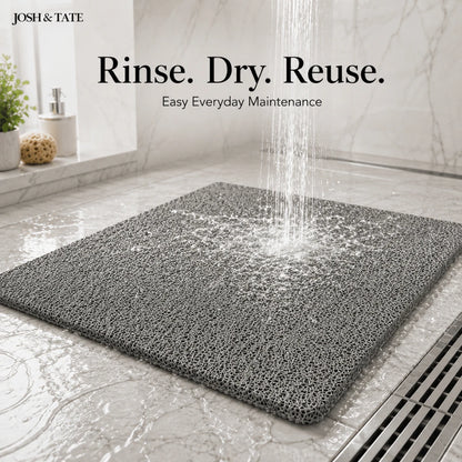 Josh & Tate - StepDry™ Anti-Slip Bath Mat - Gray bath mat on a bathroom floor with water being rinsed over it, featuring 'Josh & Tate' branding.