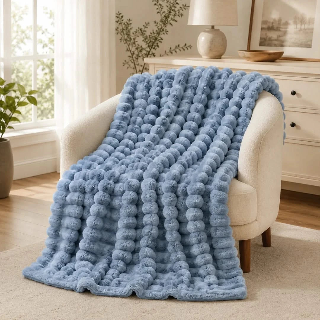 Blue textured blanket draped over a white armchair in a room with a lamp and plant.