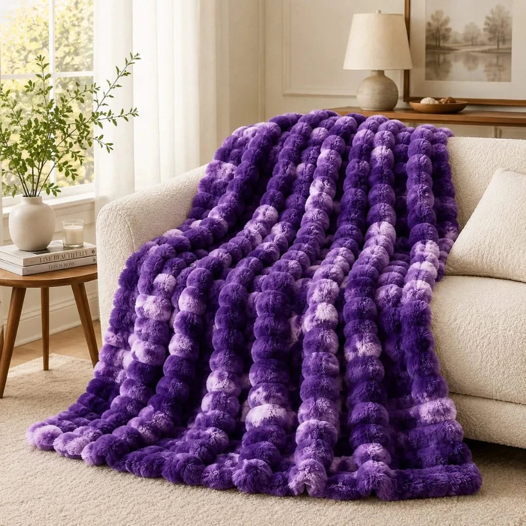 Purple textured blanket draped over a beige sofa in a living room.