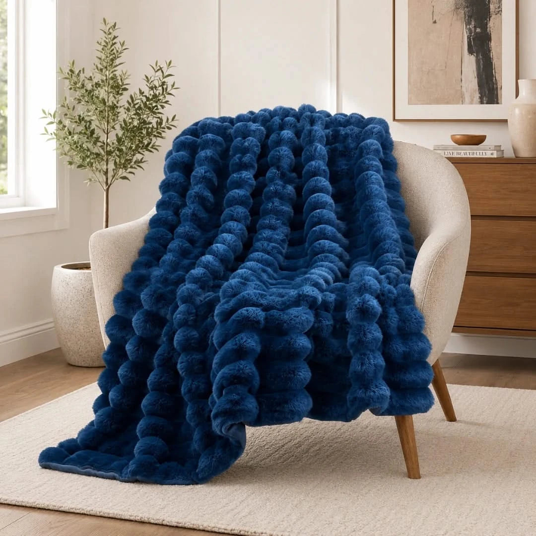 Blue textured blanket draped over a chair in a room with a plant and dresser.
