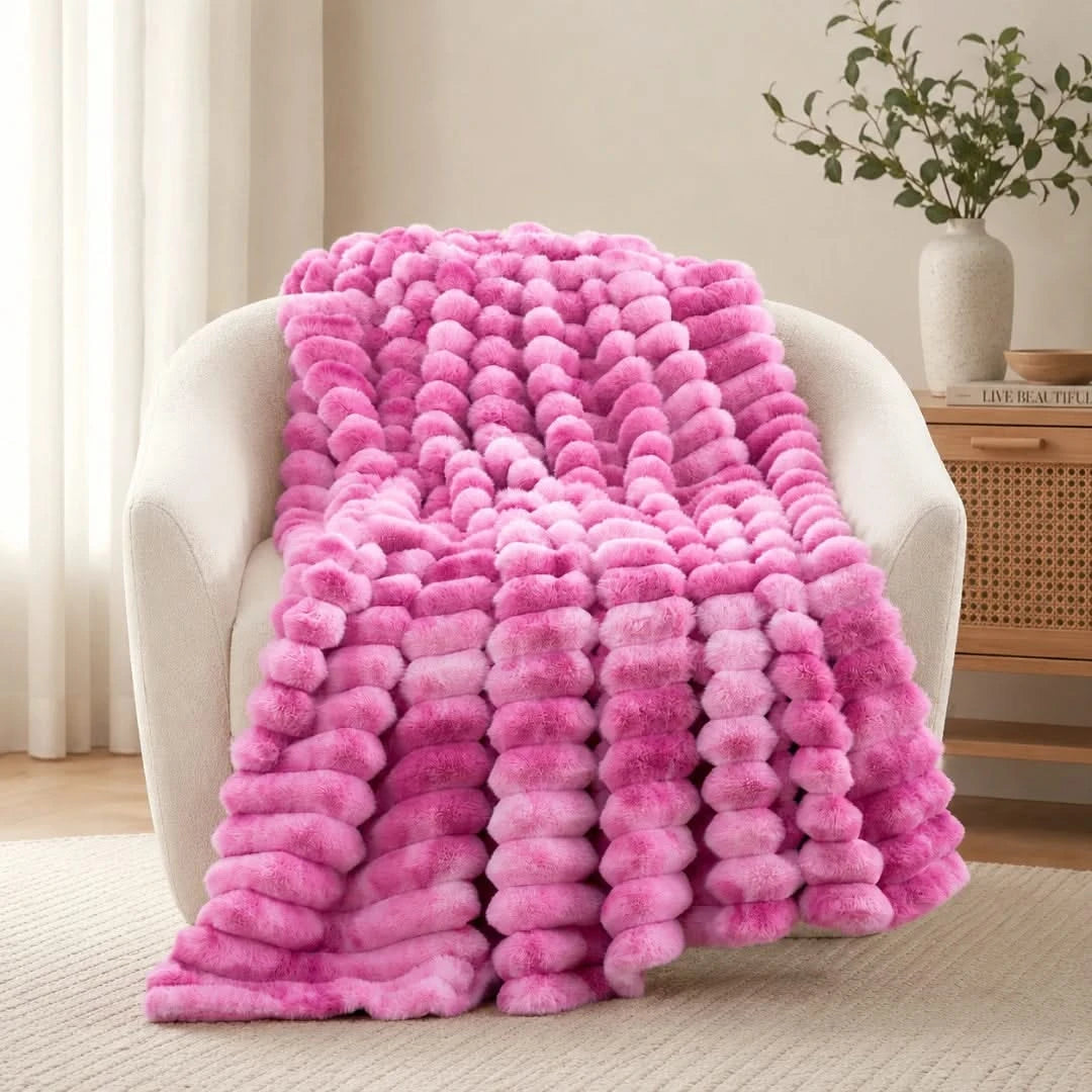 Pink ombre blanket draped over a chair in a room with a plant and wooden side table.