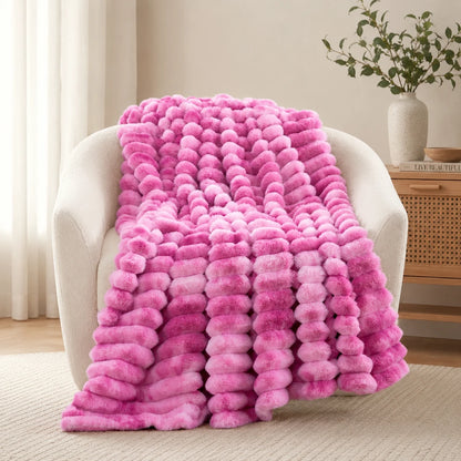 Pink ombre blanket draped over a chair in a room with a plant and wooden side table.