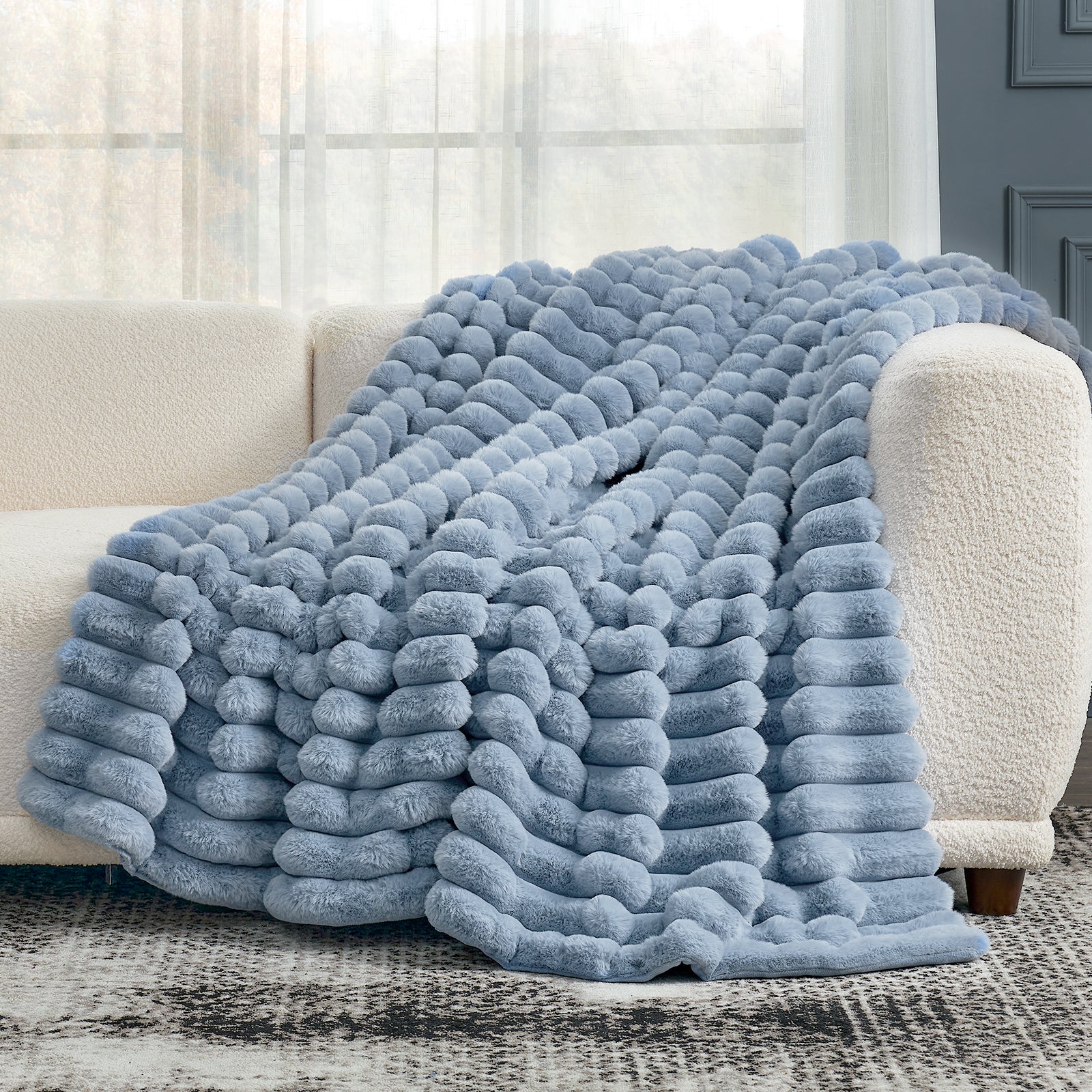 Blue textured blanket draped over a white couch in a living room setting.
