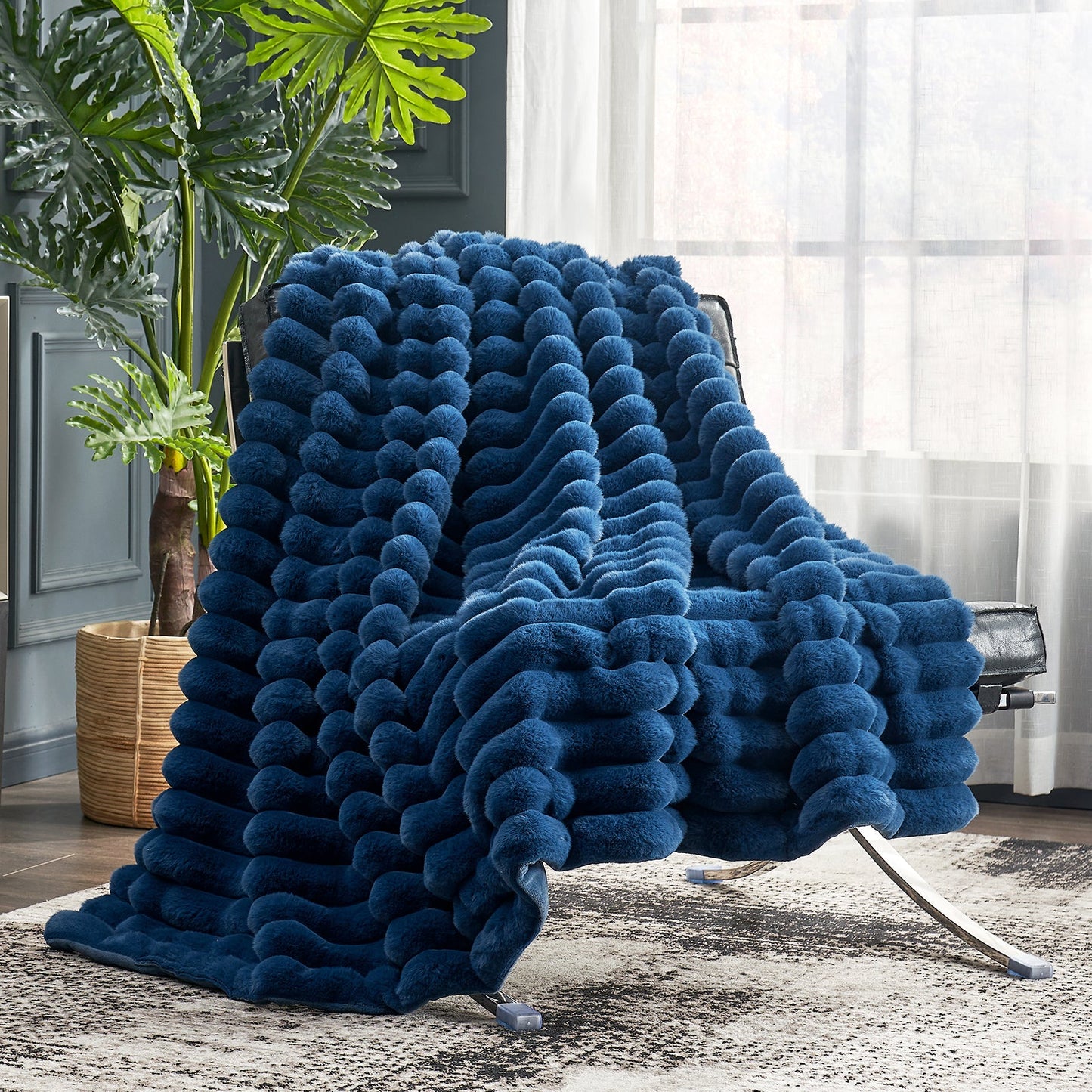 Blue textured blanket draped over a chair in a room with a plant and curtains.