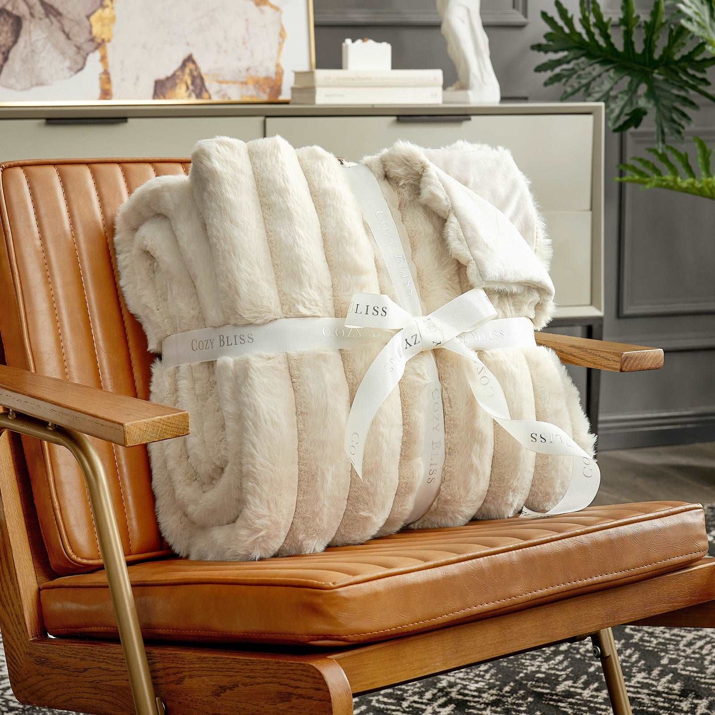 Beige plush blanket with a white ribbon on a brown leather chair.
