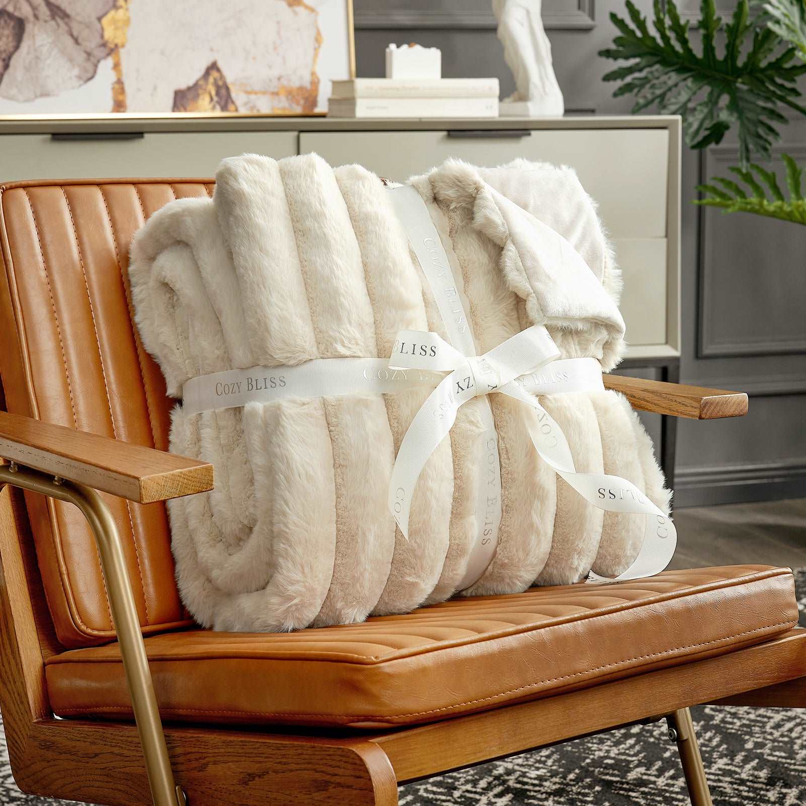 Beige plush blanket with a white ribbon on a brown leather chair.