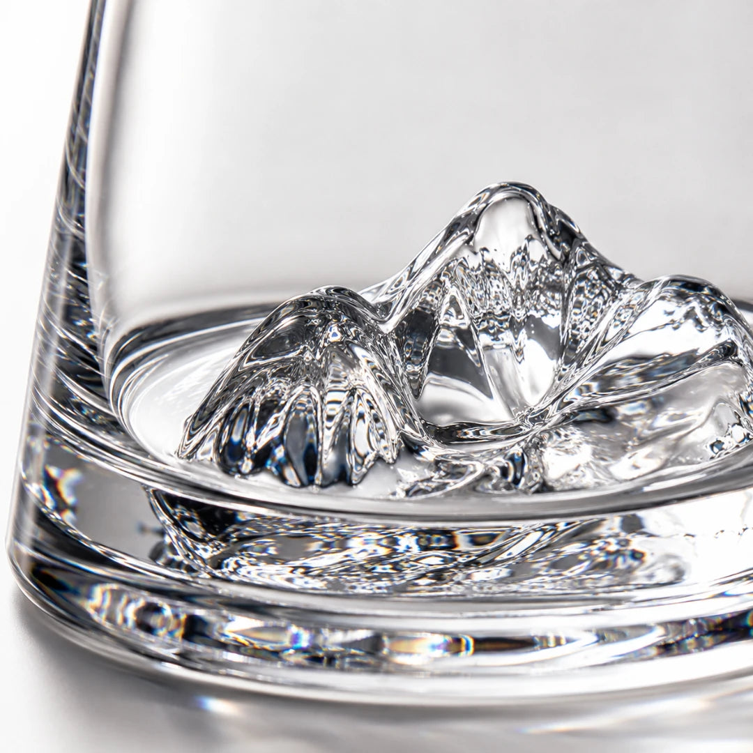 Josh & Tate - SummitRock™ Crystal Whiskey Glass - A close-up of a clear glass tumbler with a sculptural mountain-shaped ice cube resting inside the glass against a bright white background.