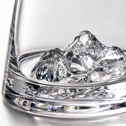 Josh & Tate - SummitRock™ Crystal Whiskey Glass - A close-up of a clear glass tumbler with a sculptural mountain-shaped ice cube resting inside the glass against a bright white background.