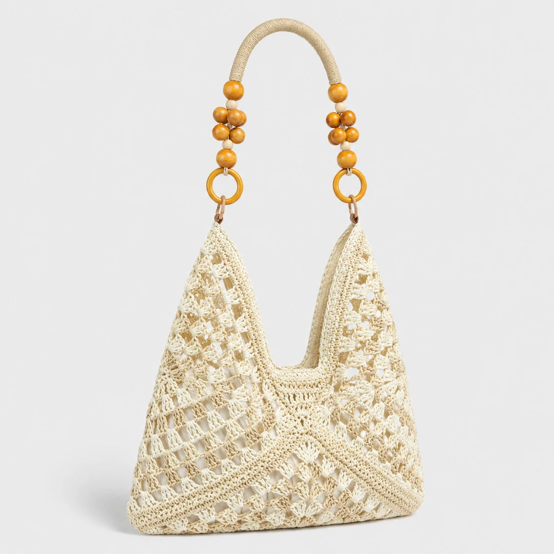 Josh & Tate - SunWeave™ Crochet Hobo Bag - A cream-colored crochet shoulder bag with a textured openwork pattern, featuring a curved top handle adorned with wooden beads and gold-tone rings, set against a light gray background.