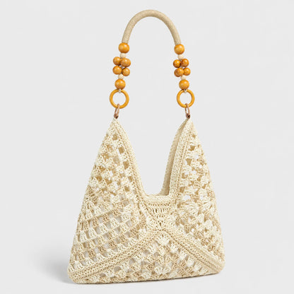 Josh & Tate - SunWeave™ Crochet Hobo Bag - A cream-colored crochet shoulder bag with a textured openwork pattern, featuring a curved top handle adorned with wooden beads and gold-tone rings, set against a light gray background.