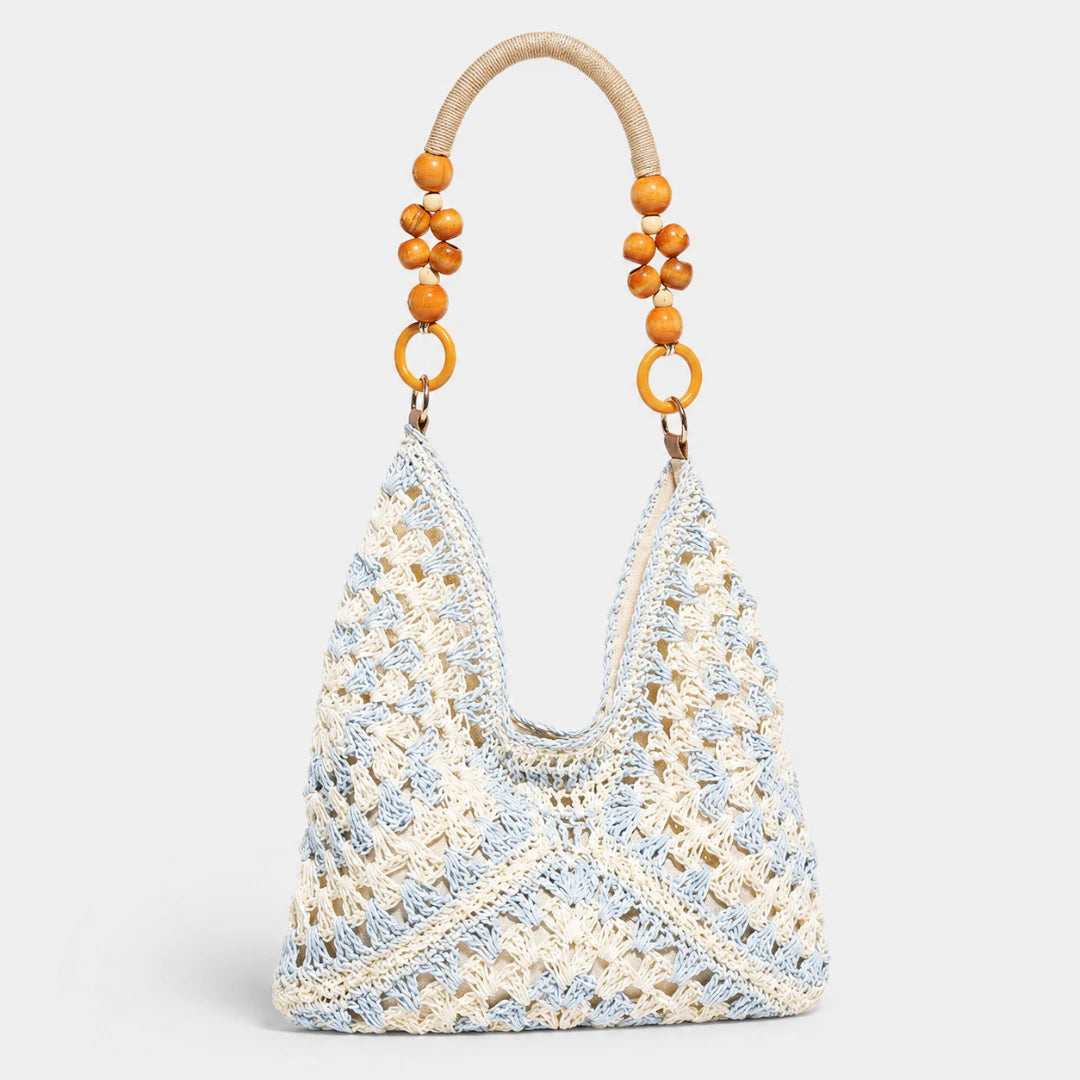 Josh & Tate - SunWeave™ Crochet Hobo Bag - A crocheted shoulder bag in cream and light blue with a curved natural wood handle adorned with orange wooden beads, shown against a light gray background.