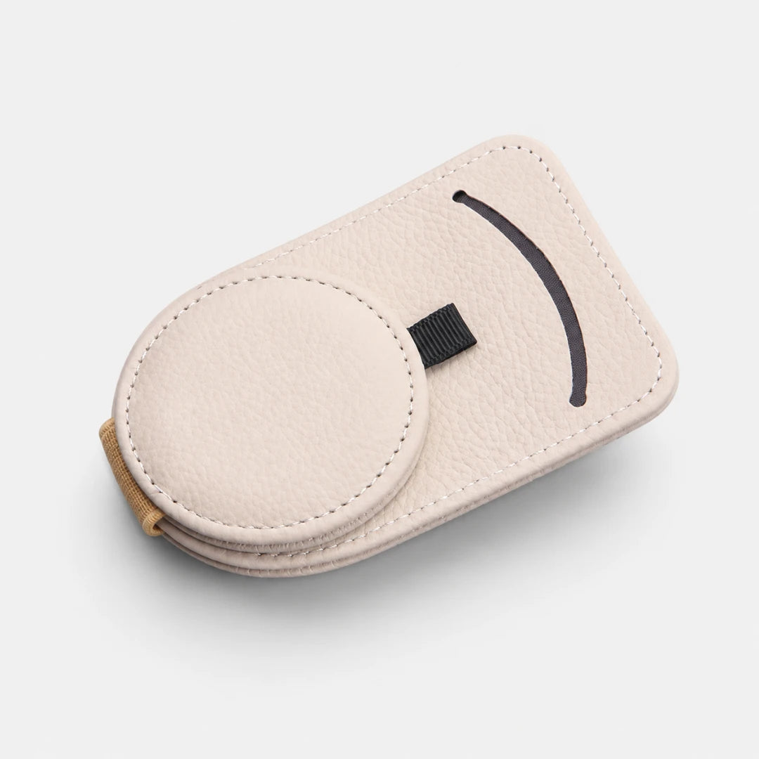 Josh & Tate - SunglassClip™ Car Visor Organizer - A light beige pebbled leather magnetic phone case with a circular magnetic ring, a black curved accent cutout, and a small black strap, shown on a light gray background.