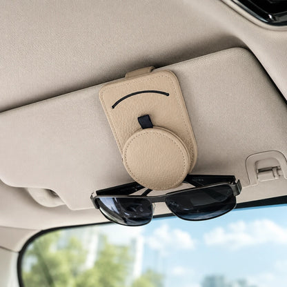 Josh & Tate - SunglassClip™ Car Visor Organizer - A beige sun visor holder with a smiley face design and a circular magnetic card slot, mounted on a car's sun visor with sunglasses resting underneath.