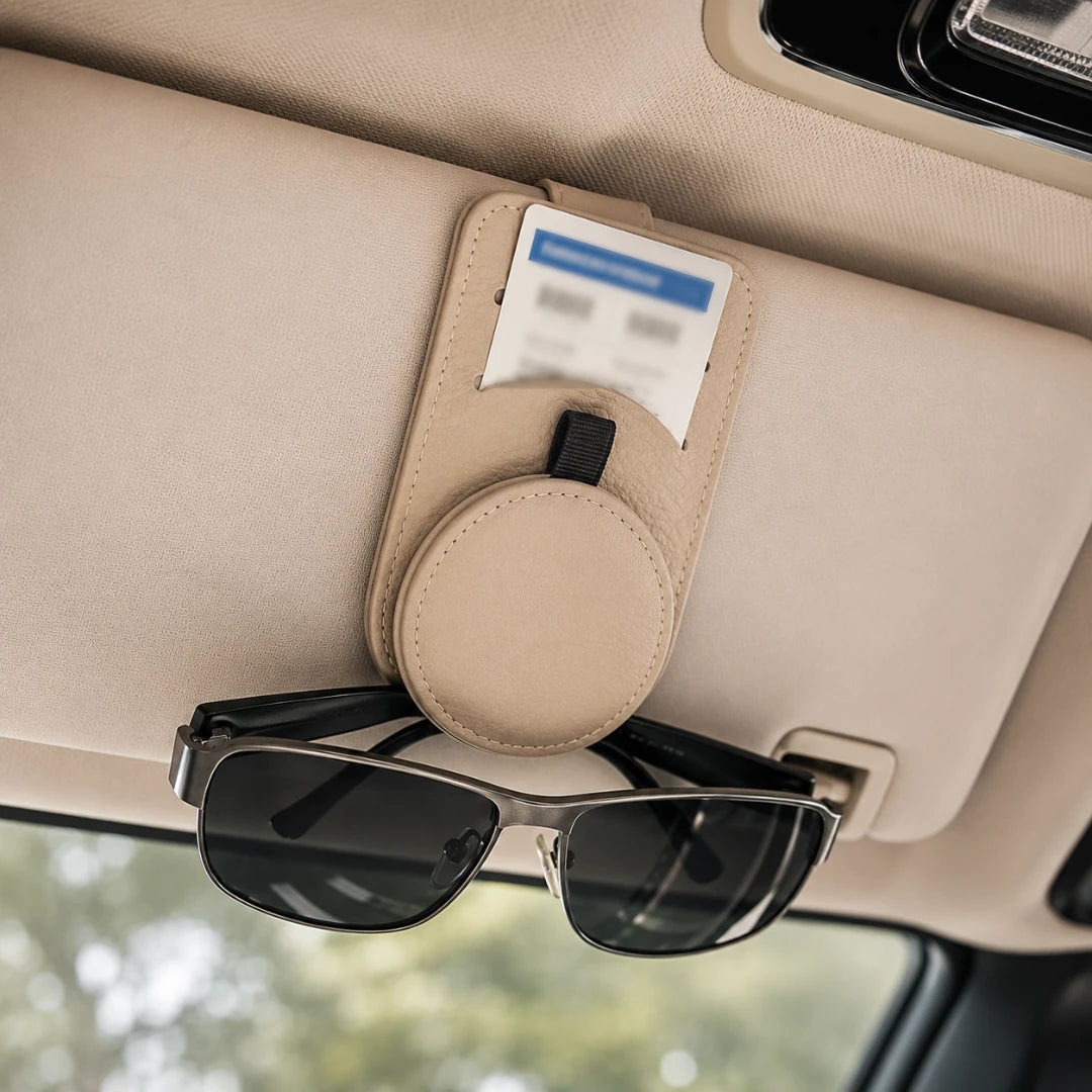 Josh & Tate - SunglassClip™ Car Visor Organizer - A beige car sun visor organizer clip mounted on a beige car sun visor, holding a card in its slot and a pair of black sunglasses in front.