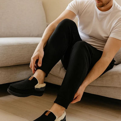 Person sitting on a couch wearing black loafers with white soles.